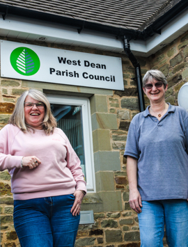 Two smiling staff members from West Dean Parish Council in Bream photographed outside their office under the Parish Council sign