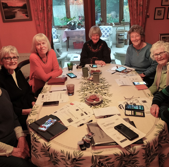 Photo of a group of older people meeting round a table to support each other with using tech devices