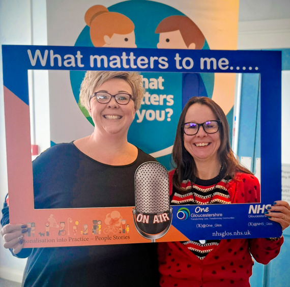 Jo Main and Karen Price photographed looking through a big cardboard photo frame titled "What Matters To You"