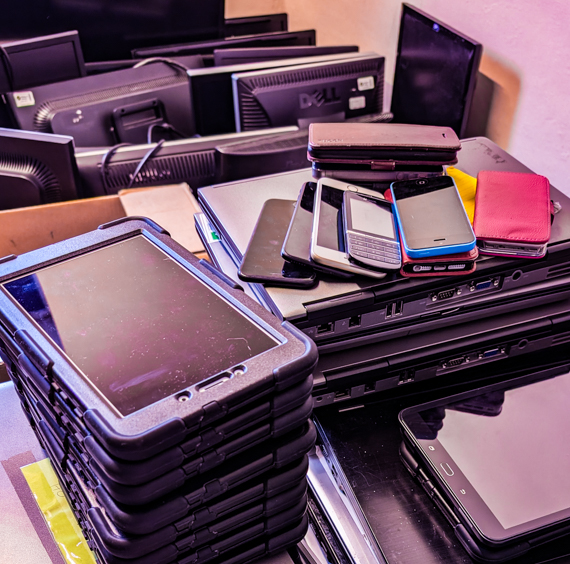 photo of stacks of used laptops, tablets and phones, awaiting refurbishment