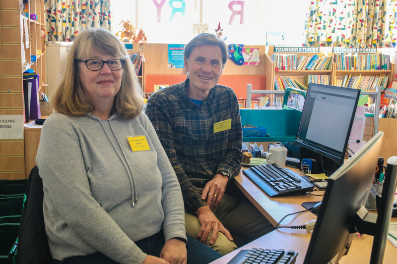 Library volunteers Helen and Phil sitting at the library enquiry desk.