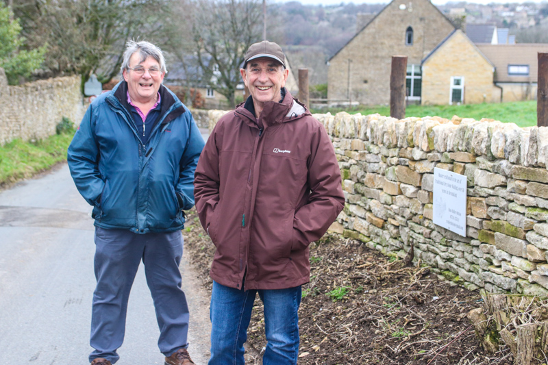 Two men in anoraks standing next to a newly re-built section of dry stone walling on a lane in Frampton Mansell