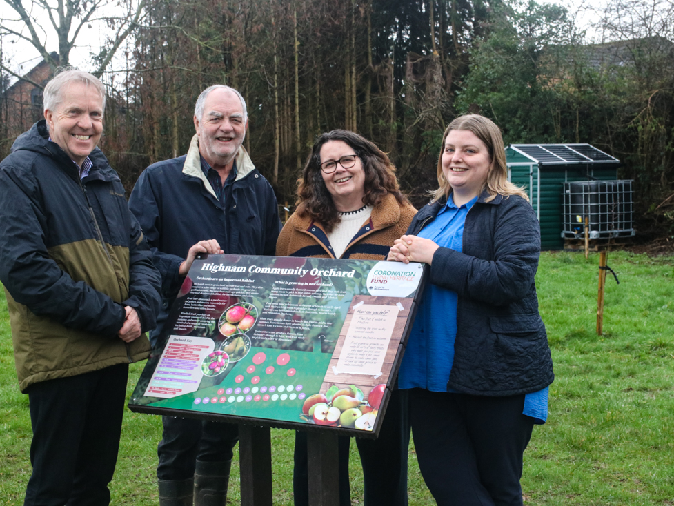 Parish Council and GRCC representatives standing in front of a colourful sign / interpretation board in the village's community orchard